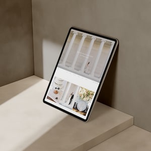 Może przedstawiać: Tablet wyświetlający stronę internetową firmy fotograficznej specjalizującej się w fotografii ślubnej, o nazwie "Millie Photography". Strona zawiera zdjęcia pary ślubnej, tortu weselnego i kompozycji kwiatowych.