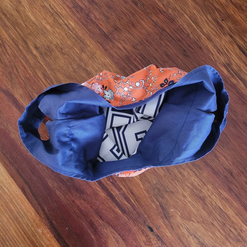 Navy blue bag from above on wooden surface. Bag is scrunched down and open to show netball bib lettering on inside. Print on outside is orange floral.