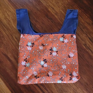Bag turned inside out to show print lining on reverse. Print is orange floral. Bag is laid out flat on wooden surface. The bag’s short straps are navy blue.