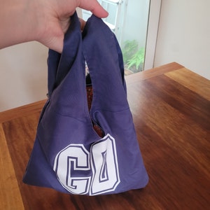 Navy blue bag with white lettering GD. A hand is holding the bag by its short straps.