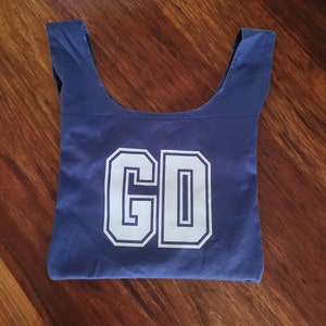 Navy blue bag with yellow letting, GD. Bag is laid out flat on wooden surface and looks like a normal netball bib.