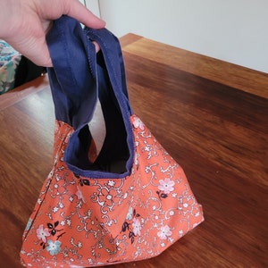 Netball bib bag reversed with orange floral lining on outside.  A hand is holding the bag by its navy blue straps.