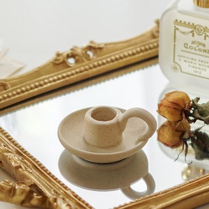 dotted beige ceramic taper candle holder, yellow rose dried flowers, and santa maria novella perfume placed on rectangular gold french mirror tray on white table