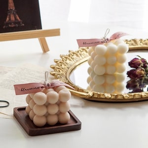 There is France Paris Eiffel Tower poster, soy wax handmade candlestick taper candle with ceramic candle holder, square bubble cube candle with neutral color, dried flower and french style vanity mirror on table.