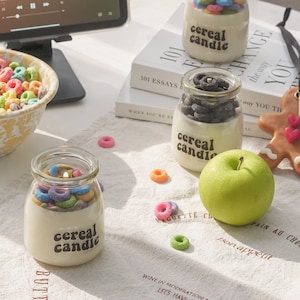 a lit colorful cereal candle, fruit loops wax melts, a green apple, oreo candle, gingerbread scented wax placed on kitchen cotton fabric, yellow crow canyon salad bowl filled with froot loops, and ipad mini.