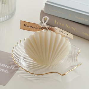 a neutral tone grey tone down colors of aesthetic books, you smell like love text post card, clear transparent and gold finished detail textured seashell candle holder or jewelry dish tray with white minimal seashell candle with beige ribbon on top.