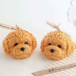 two of very detailed cute golden doodle, poodle and bichon dog-shaped soy wax candles are displayed on the table.