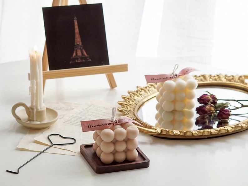 There is France Paris Eiffel Tower poster, soy wax handmade candlestick taper candle with ceramic candle holder, square bubble cube candle with neutral color, dried flower and french style vanity mirror on table.