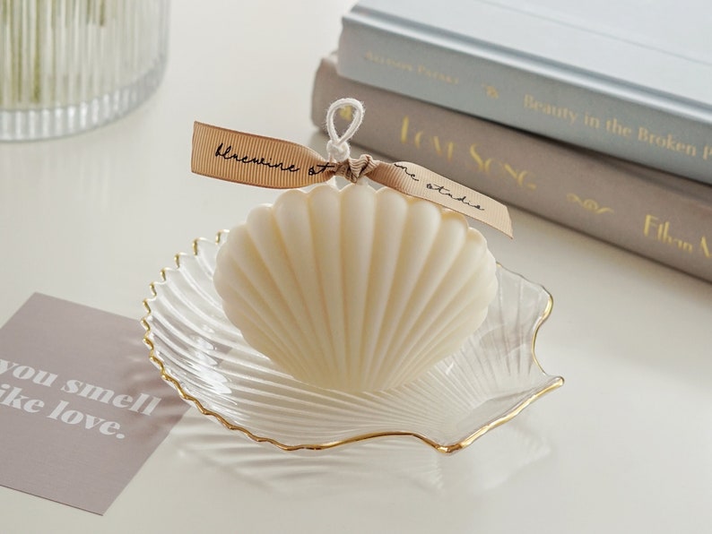 a neutral tone grey tone down colors of aesthetic books, you smell like love text post card, clear transparent and gold finished detail textured seashell candle holder or jewelry dish tray with white minimal seashell candle with beige ribbon on top.