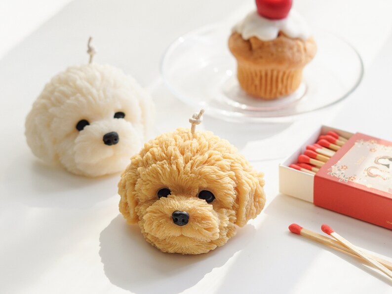 goldendoodle soy pillar candle, white bichon soy pillar candle, cherry muffin candle on a glass plate, and matches on white table