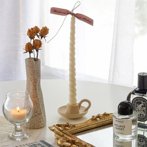 white twisted swirl soy pillar taper candle in a dotted beige ceramic candle holder, yellow rose dried flowers in unique vase and a lit tealight candle and Byredo Mojave Ghost and Diptyque Fleur de Peau placed on rectangular gold french mirror tray