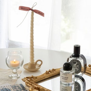 There are aesthetic items displayed on the desk like handmade soy was candle, candlestick taper candle, famous niche perfume as Byredo and Diptyque.