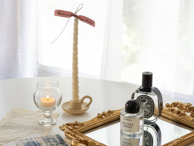 There are aesthetic items displayed on the desk like handmade soy was candle, candlestick taper candle, famous niche perfume as Byredo and Diptyque.