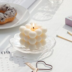 There are my favorite oreo flavor mochi donut and beautiful aesthetic minimal style white handmade soy wax bubble cube candle with heart shaped wick dipper on the table in sunlight.