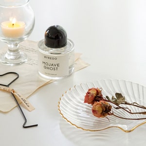 a neutral tone grey tone down colors of aesthetic books, you smell like love text post card, clear transparent and gold finished detail textured seashell candle holder or jewelry dish tray with white minimal seashell candle with beige ribbon on top.