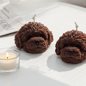 There are two dark chocolate brown color of two poodle dog shaped soy wax candle on the white round table.