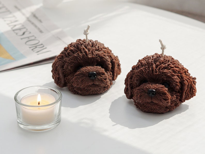 There are two dark chocolate brown color of two poodle dog shaped soy wax candle on the white round table.