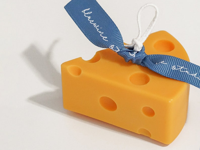 a slice of yellow cheddar cheese shape soy pillar candle with a blue bluewine studio ribbon