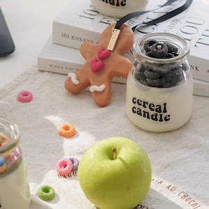 a lit colorful cereal candle, fruit loops wax melts, a green apple, oreo candle, gingerbread scented wax, 101 Essays that will change the way you think by Brianna Wiest placed on kitchen cotton fabric