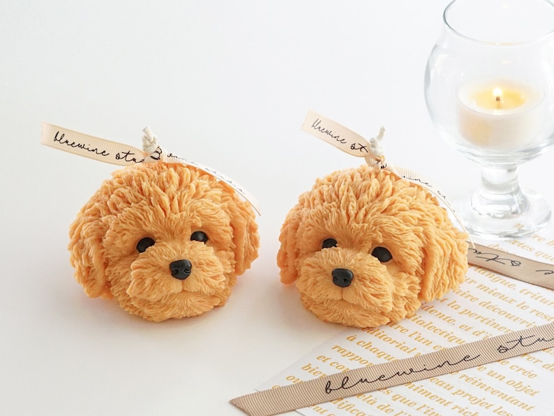 two of very detailed cute golden doodle, poodle and bichon dog-shaped soy wax candles are displayed on the table.