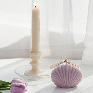 lavender seahsell soy pillar candle with dreamy aesthetic beach vibes, lavender tulips, and a lit taper candle on a clear dish