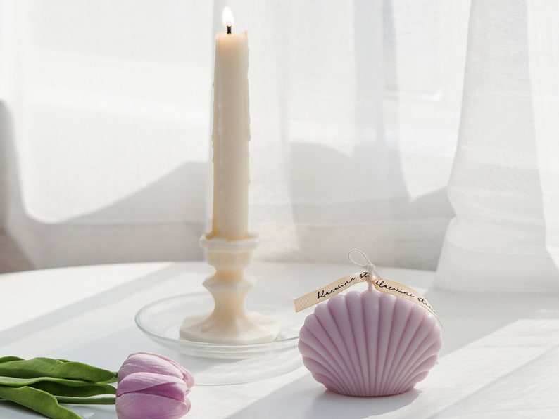 lavender seahsell soy pillar candle with dreamy aesthetic beach vibes, lavender tulips, and a lit taper candle on a clear dish