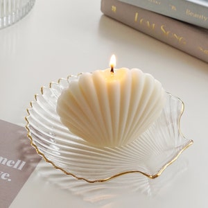 a neutral tone grey tone down colors of aesthetic books, you smell like love text post card, clear transparent and gold finished detail textured seashell candle holder or jewelry dish tray with white minimal seashell candle with beige ribbon on top.