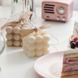 beautiful sunlight reflecting on the desk with two handmade soy wax candles with bluewine studio ribbon and sweet blueberry dessert cake displayed as minimal aesthetic and dreamy way.