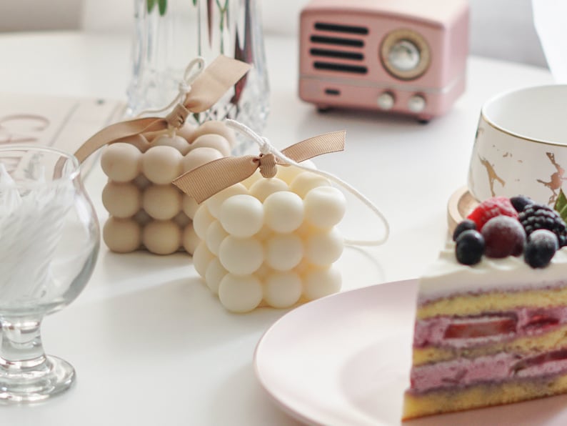 beautiful sunlight reflecting on the desk with two handmade soy wax candles with bluewine studio ribbon and sweet blueberry dessert cake displayed as minimal aesthetic and dreamy way.