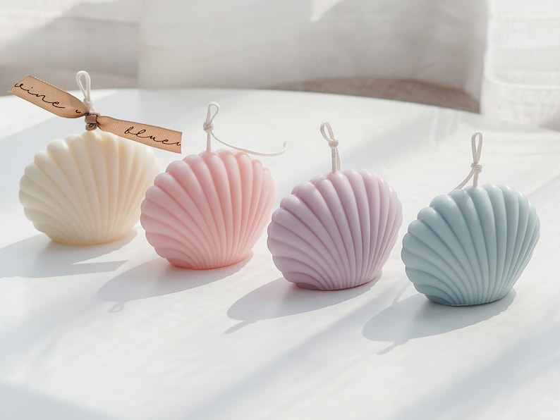 aesthetic minimal dreamy beach style mood from the back there is white, pink, lavender purple and mint blue color of soy wax seashell shaped candle in order with beige ribbon on the white minimal round table.