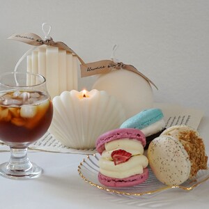 three macarons on a gold rim seashell clear tray, iced americano in a mini glass, a lit seashell soy pillar candle, ribbed stair candle and round sphere candle with beige bluewine studio ribbons giving that dreamy minimal aesthetic vibes