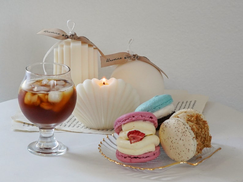 three macarons on a gold rim seashell clear tray, iced americano in a mini glass, a lit seashell soy pillar candle, ribbed stair candle and round sphere candle with beige bluewine studio ribbons giving that dreamy minimal aesthetic vibes