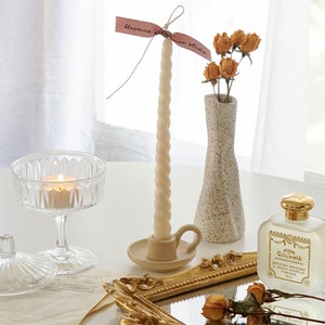 white twisted swirl soy pillar taper candle in a dotted beige ceramic candle holder, yellow rose dried flowers in unique vase and a lit tealight candle and Byredo Mojave Ghost and Diptyque Fleur de Peau placed on rectangular gold french mirror tray