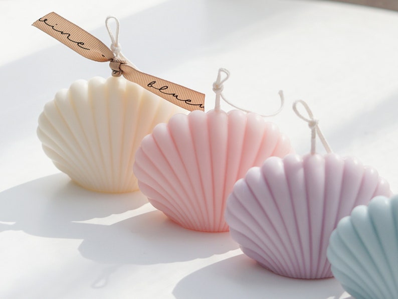 aesthetic minimal dreamy beach style mood from the back there is white, pink, lavender purple and mint blue color of soy wax seashell shaped candle in order with beige ribbon on the white minimal round table.