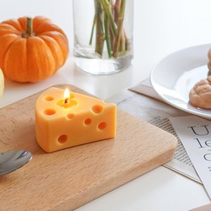 a lit yellow cheese shape soy pillar candle on ikea mini wood board, cookie candles on white ceramic plate, yellow and orange pumpkins, and magazine papers