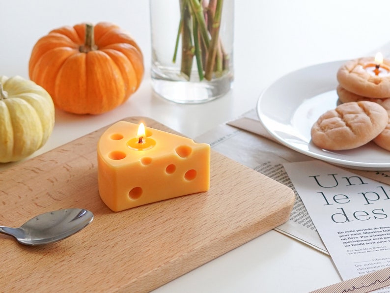 a lit yellow cheese shape soy pillar candle on ikea mini wood board, cookie candles on white ceramic plate, yellow and orange pumpkins, and magazine papers