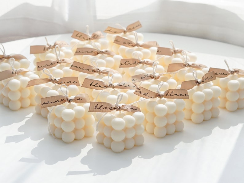 twenty white cube bubble square soy pillar candle with beige bluewine studio ribbon are placed on white round table for party favors