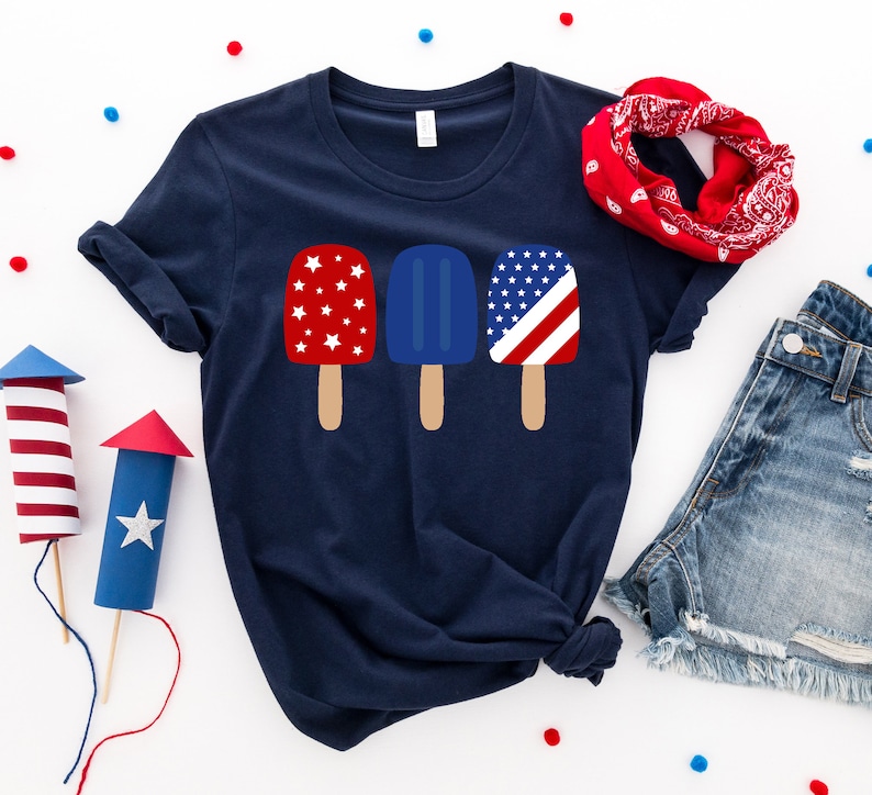 May include: A navy blue t-shirt with a graphic of three popsicles. The popsicles are red, white, and blue and have a star pattern.