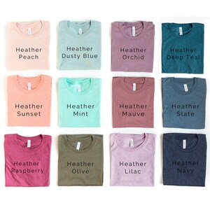 May include: Twelve folded t-shirts in various heather colors, including peach, dusty blue, orchid, deep teal, sunset, mint, mauve, slate, raspberry, olive, lilac, and navy.