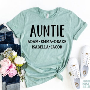 May include: A light blue t-shirt with the word "AUNTIE" in black text and the names "ADAM", "EMMA", "DRAKE", "ISABELLA", and "JACOB" printed below in black text.