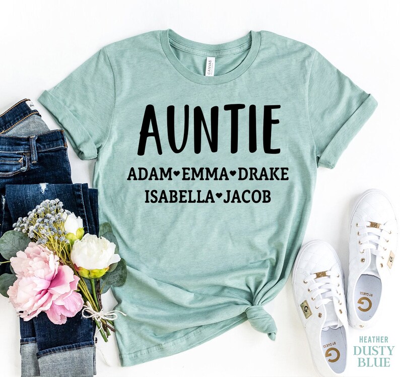 May include: A light blue t-shirt with the word "AUNTIE" in black text and the names "ADAM", "EMMA", "DRAKE", "ISABELLA", and "JACOB" printed below in black text.
