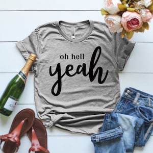 May include: Gray t-shirt with the text "oh hell yeah" in black cursive lettering.