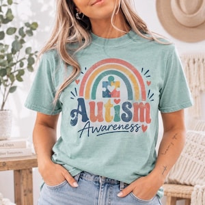 A woman wearing a light blue t-shirt with a colorful graphic design that says "Autism Awareness" and a rainbow symbol.