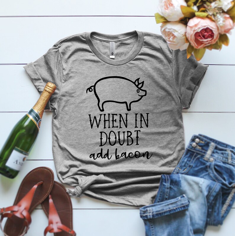 K&ouml;nnte beinhalten: Ein graues T-Shirt mit einer schwarzen Schweineillustration und dem Text "When in doubt add bacon".
