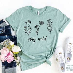 May include: A light blue t-shirt with a black floral design and the text "stay wild".