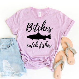 May include: A light purple t-shirt with the text "Bitches catch fishes" in black lettering and a silhouette of a fish.