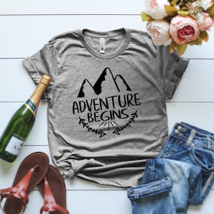 May include: Gray t-shirt with a black graphic of mountains and the text "Adventure Begins".