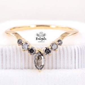 May include: A gold band ring with a marquise-shaped grey diamond in the center and smaller round grey diamonds on the band. The ring is set in a V-shape and the text "Rubysta Jewels" is visible on the band.