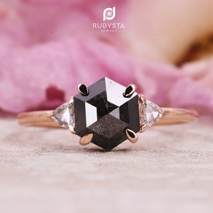 May include: A rose gold engagement ring with a black hexagonal diamond and two smaller triangular diamonds on either side.