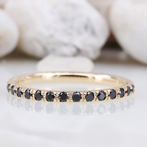 May include: A thin gold band ring featuring a continuous row of small, round, faceted black stones set in a shared prong setting. The metal has a polished finish, and the stones are evenly spaced along the entire circumference of the ring.